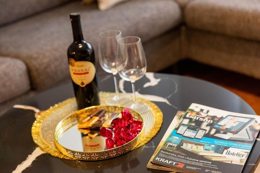 A bottle of wine, two glasses, a plate with chocolates, and a magazine on a table.