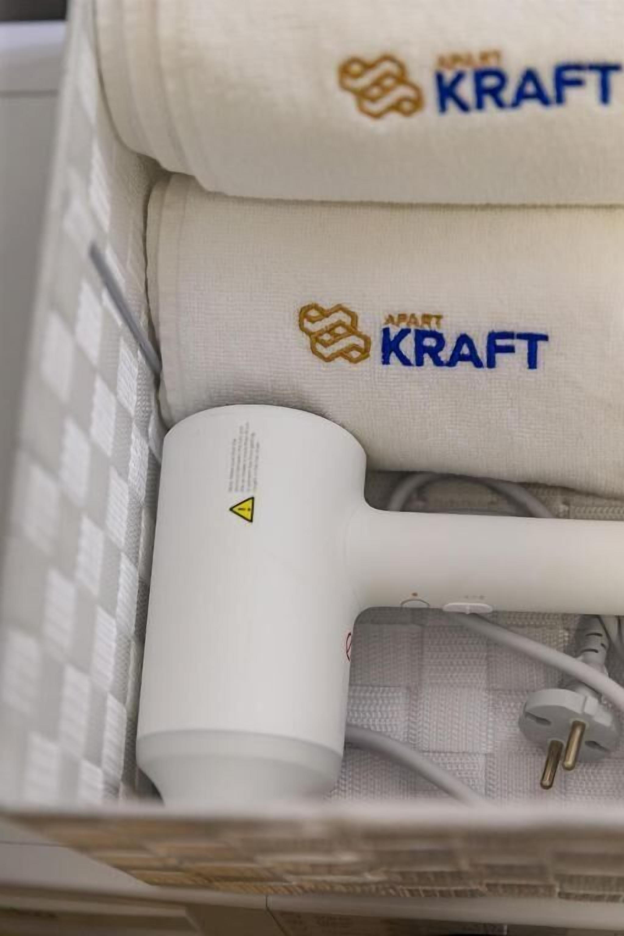 A white portable hair dryer with a warning label, a white power cord, and a white fabric with embroidered text.