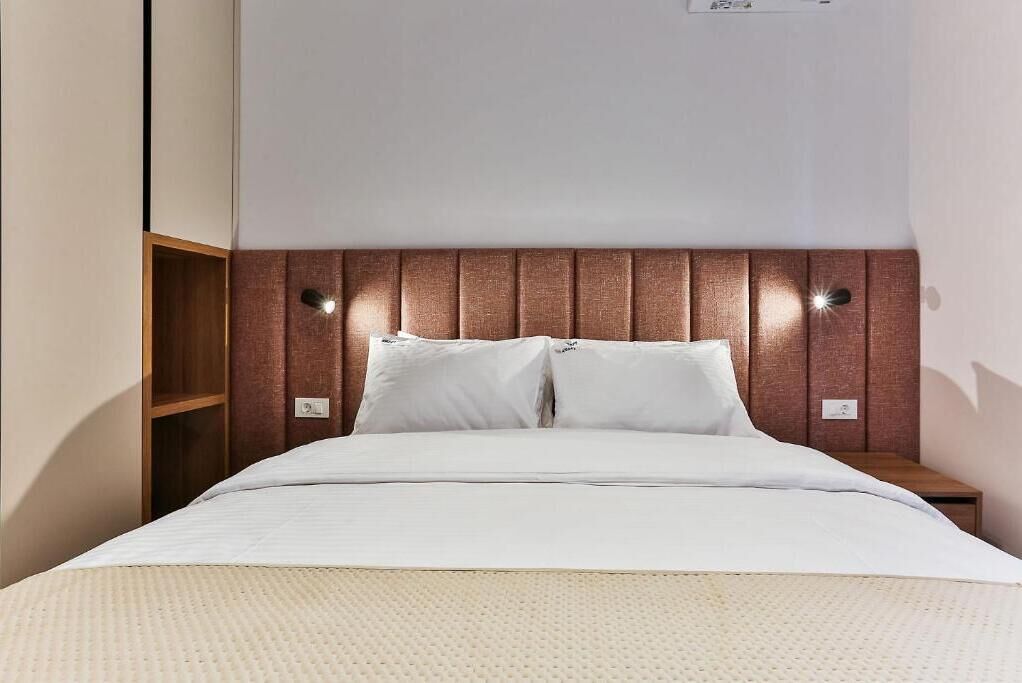 A neatly made bed with a wooden headboard, two bedside tables, and a wall-mounted light fixture.