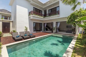 Une maison moderne à deux étages, dotée d’une piscine, de mobilier d’extérieur et d’un balcon agrémenté de plantes.