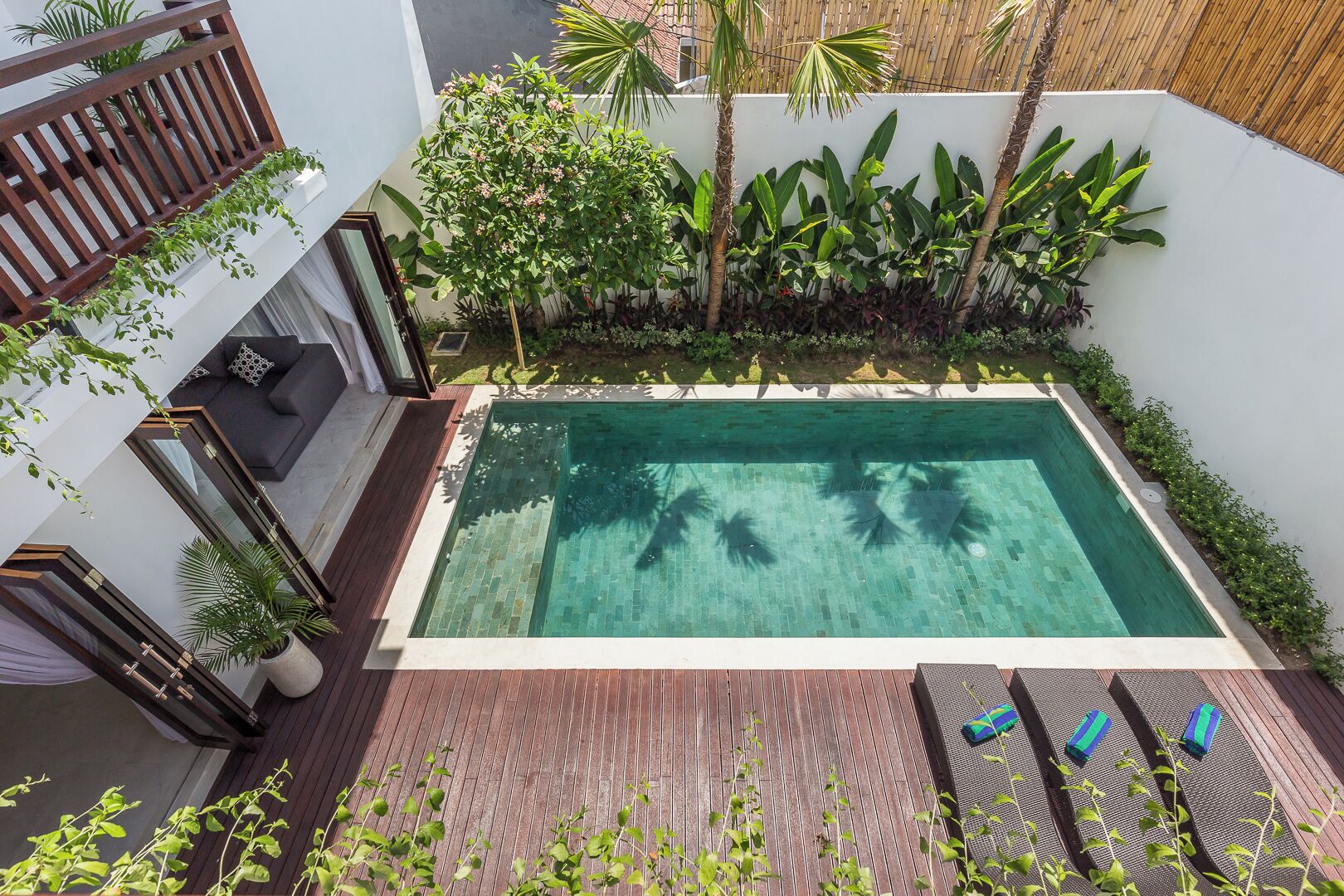 Une piscine rectangulaire bordée de carreaux, entourée d’une végétation luxuriante et dotée d’une terrasse en bois.