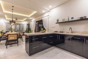 Une cuisine moderne avec des meubles de couleur noire, un plan de travail en marbre et un coin repas avec une table dressée pour quatre personnes.