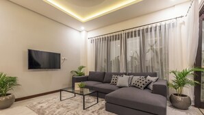 A modern living room with a grey sofa, a glass coffee table, and two potted plants. - Villa Azura Seminyak (Badung)