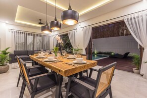 Un espace repas avec une table en bois, des chaises noires et des lampes suspendues.