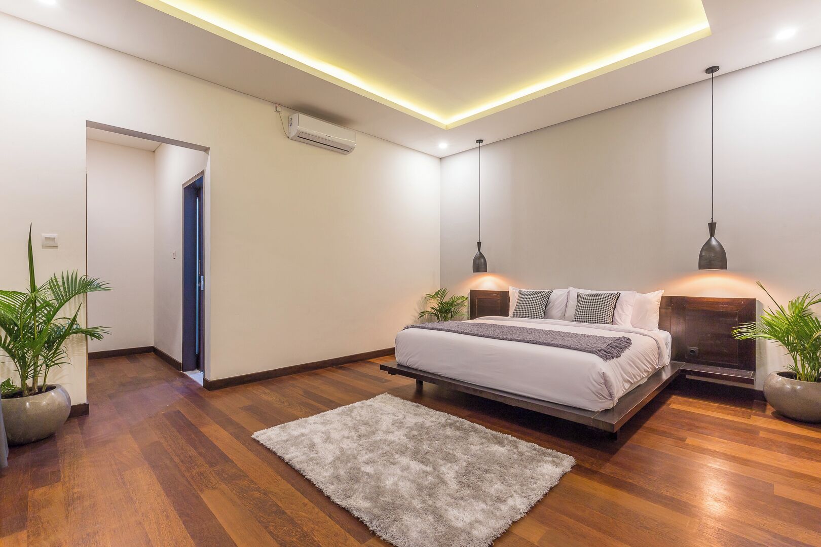 Ein modernes Schlafzimmer mit einem Bett, Nachttischen, Pendelleuchten und einer großen Kübelpflanze.