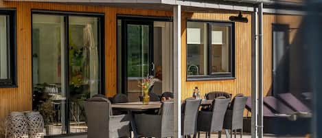 An outdoor seating area with a wooden pergola, wicker chairs, and a table with a vase of flowers.