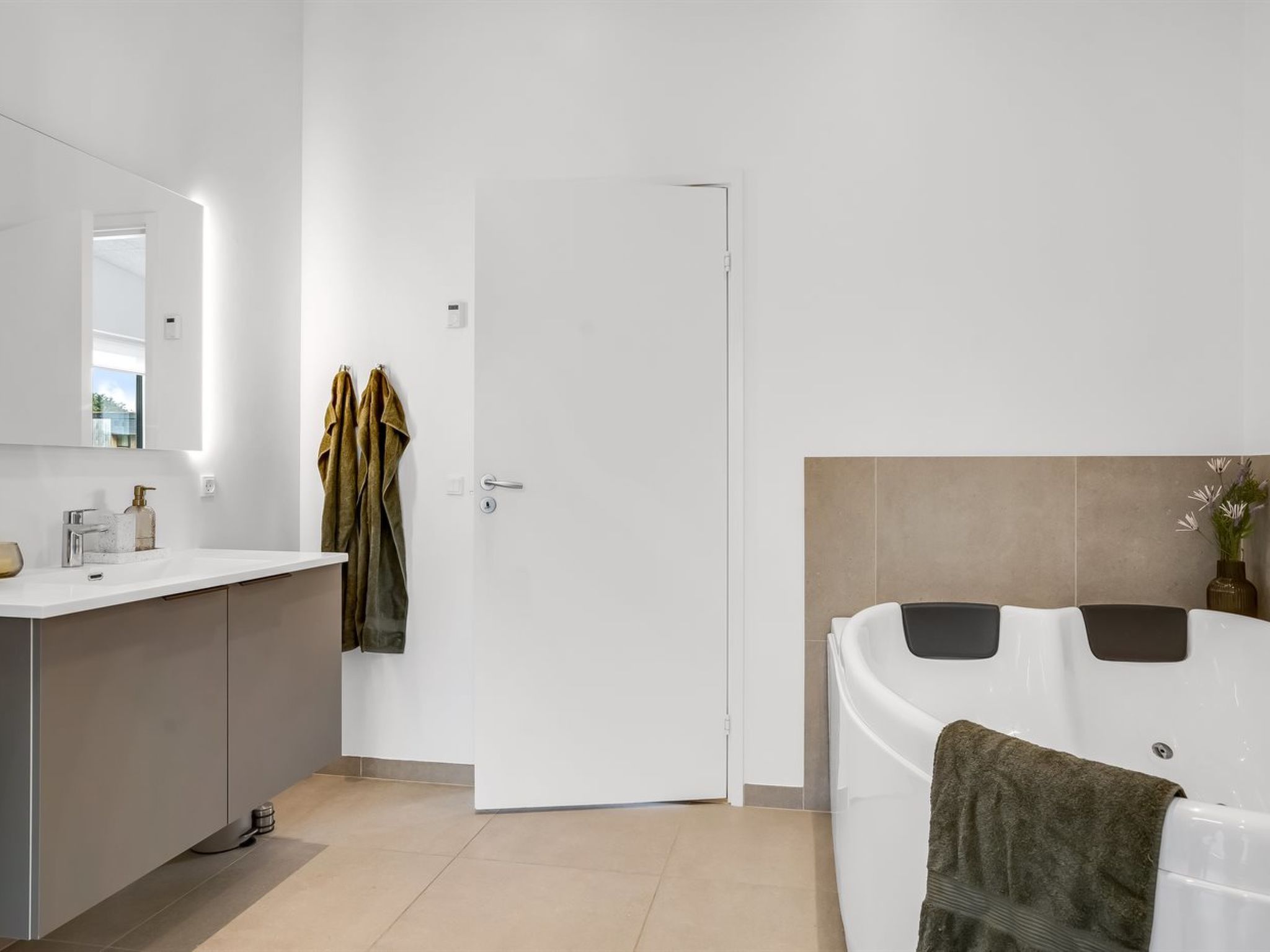 Ein modernes Badezimmer mit Waschbecken, großem Spiegel, Handtuchhalter, Tür und einer Badewanne mit Handtuch.