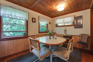 A dining area with a round table, four chairs, and a window with a view of trees.