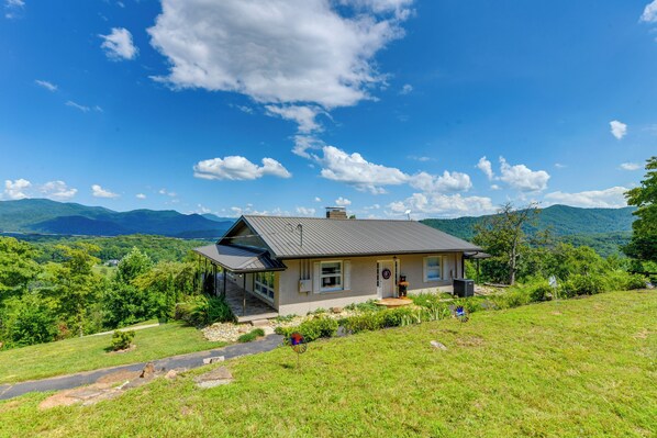 Una casa a due piani con un portico coperto, un vialetto in pietra che conduce all'ingresso e una vista sulle montagne sullo sfondo.