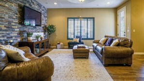 A living room with a stone wall, leather sofas, a flat-screen TV, and a large window. - Santa Teresa Retreat w/ Outdoor Fireplace (Santa Teresa)