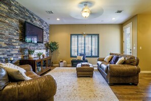 A living room with a stone wall, leather sofas, a flat-screen TV, and a large window. - Santa Teresa Retreat w/ Outdoor Fireplace (Santa Teresa)