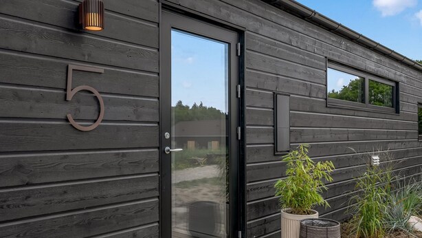 A modern building with a black exterior, a glass door, and a wooden deck.