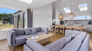 A spacious living area with a grey sofa set, a wooden coffee table, and a dining area with a wooden table and chairs.