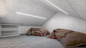 A room with a sloped ceiling, white walls, and a grey carpet. There are two large bean bags with red tags.