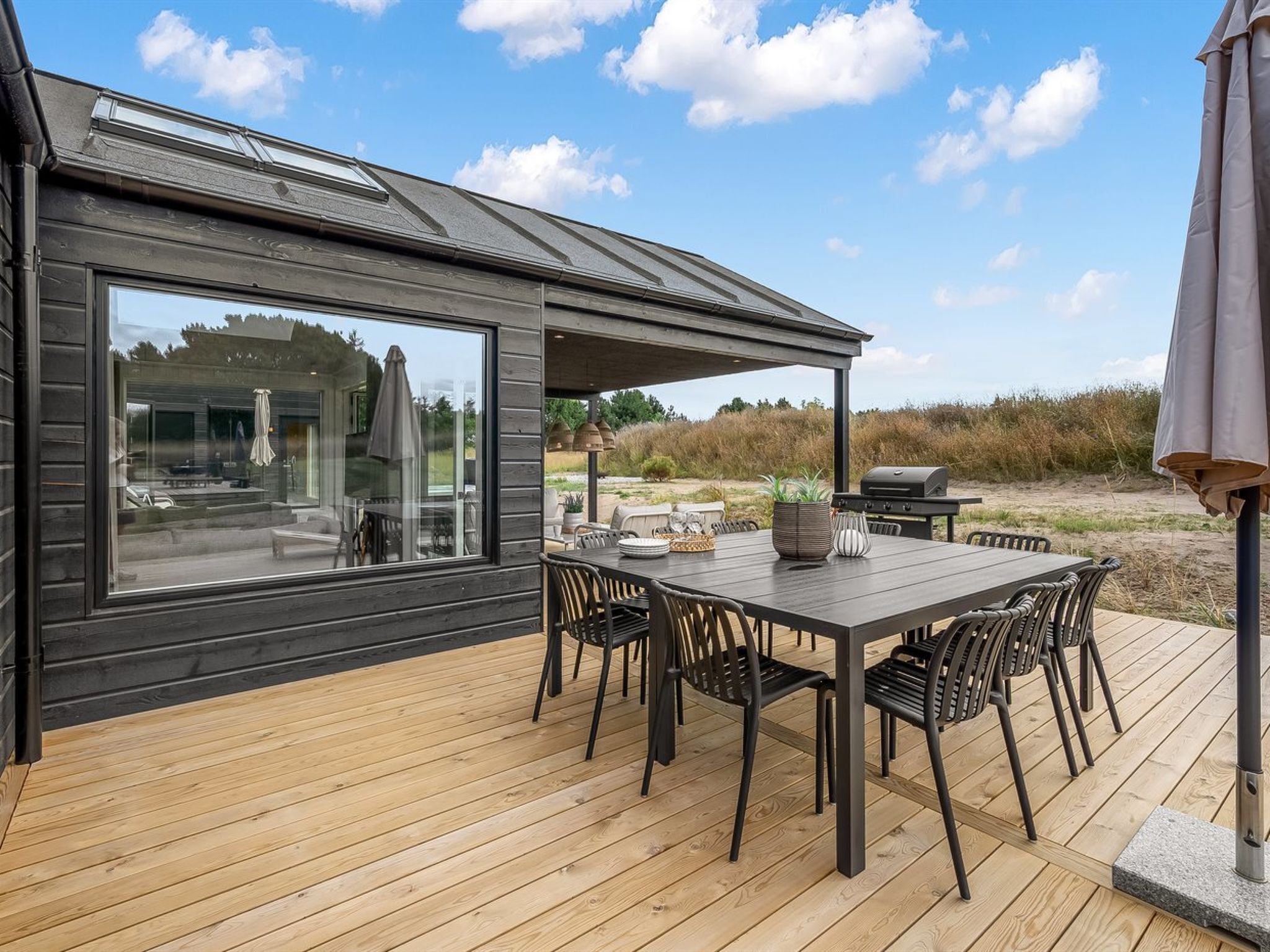 A deck with a table and chairs, a grill, and a view of the landscape.
