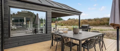 A deck with a table and chairs, a grill, and a view of the landscape.