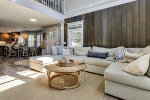 A spacious living room with a large sofa, a round wicker coffee table, and a dining area with chairs and a table. - Walk to Old Town Bluffton! Family Home w/ Balcony (Bluffton)