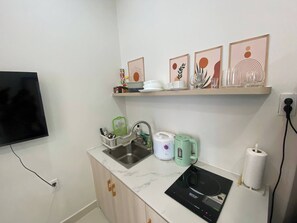 Eine Küche mit Spüle, Wasserkocher, Reiskocher und Mikrowelle. Darüber hängt an der Wand ein Bild in einem Rahmen.