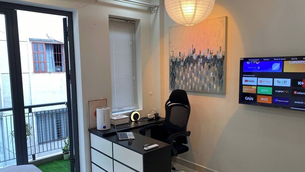 A modern office space with a desk, chair, and a mounted TV displaying various streaming services. - Cozy Studio Apartment in Prime District One, Ho Chi Minh City (Ho Chi Minh City)