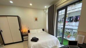 A hotel room with a bed, a desk with a laptop, a remote control, and a window with a view of a balcony. - Cozy Studio Apartment in Prime District One, Ho Chi Minh City (Ho Chi Minh City)