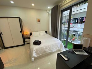 Ein Hotelzimmer mit einem Bett, einem Schreibtisch mit einem Laptop, einer Fernbedienung und einem Fenster mit Blick auf einen Balkon.