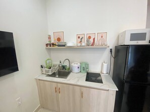 Eine kleine Küche mit Spüle, Mikrowelle, Kühlschrank und einer Arbeitsplatte mit verschiedenen Küchenutensilien.
