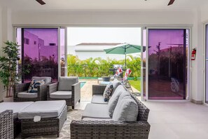 Ein modernes Wohnzimmer mit Korbmöbeln, einem Pool und Blick auf einen grünen Garten durch Glastüren.
