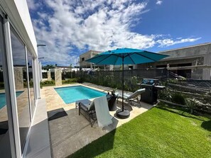 Un jardin avec une piscine, un barbecue et un espace salon abrité.