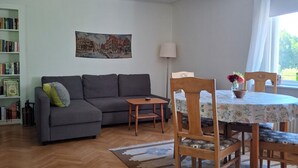 A living room with a sofa, a small table, a dining table with chairs, a lamp, and a painting on the wall.