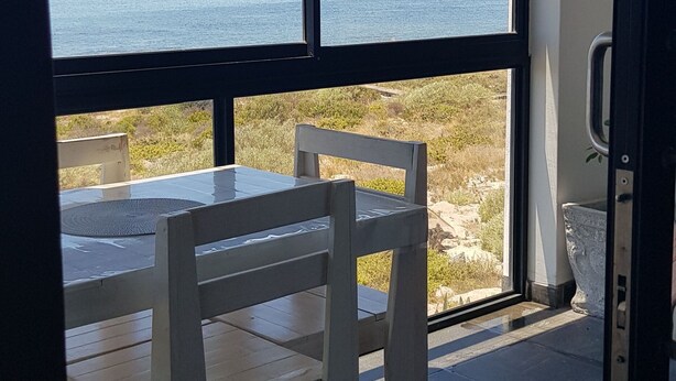 A room with a large window overlooking a body of water, a wooden table with chairs, and a tiled floor. - Beachfront Accommodation (West Coast District Municipality)