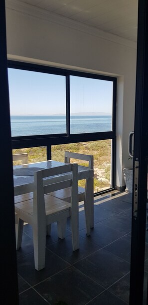 A room with a large window overlooking a body of water, a wooden table with chairs, and a tiled floor.
