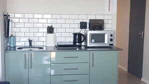 A compact kitchen with a microwave, kettle, and cabinets. - Beachfront Accommodation (West Coast District Municipality)