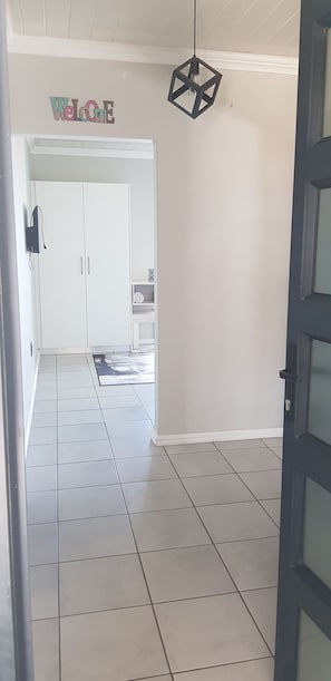 Un pasillo con suelo de baldosas, un cartel de bienvenida, una lámpara colgante de diseño geométrico y una puerta que da a una habitación.