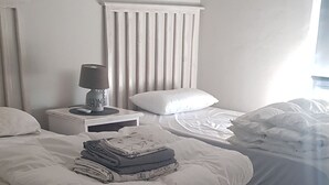 A bedroom with two beds, a bedside table with a lamp, and a radiator. - Beachfront Accommodation (West Coast District Municipality)