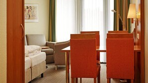 A hotel room with a bed, a sofa, a dining table with chairs, a lamp, and a window with curtains. - 4 Person Holiday Park Home in Willingen (Willingen)