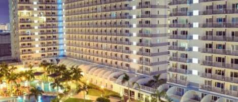 A multi-story hotel with a swimming pool and palm trees.