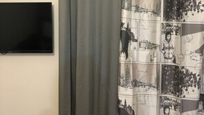 A bathroom with a grey shower curtain, a mounted flat-screen TV, and a white radiator. - Amazing Studio 11 minutes wak from Center (Thessaloniki)