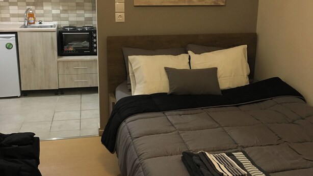 A bedroom with a bed, pillows, a bedside table, a small kitchenette with a microwave, and a painting on the wall. - Amazing Studio 11 minutes wak from Center (Thessaloniki)