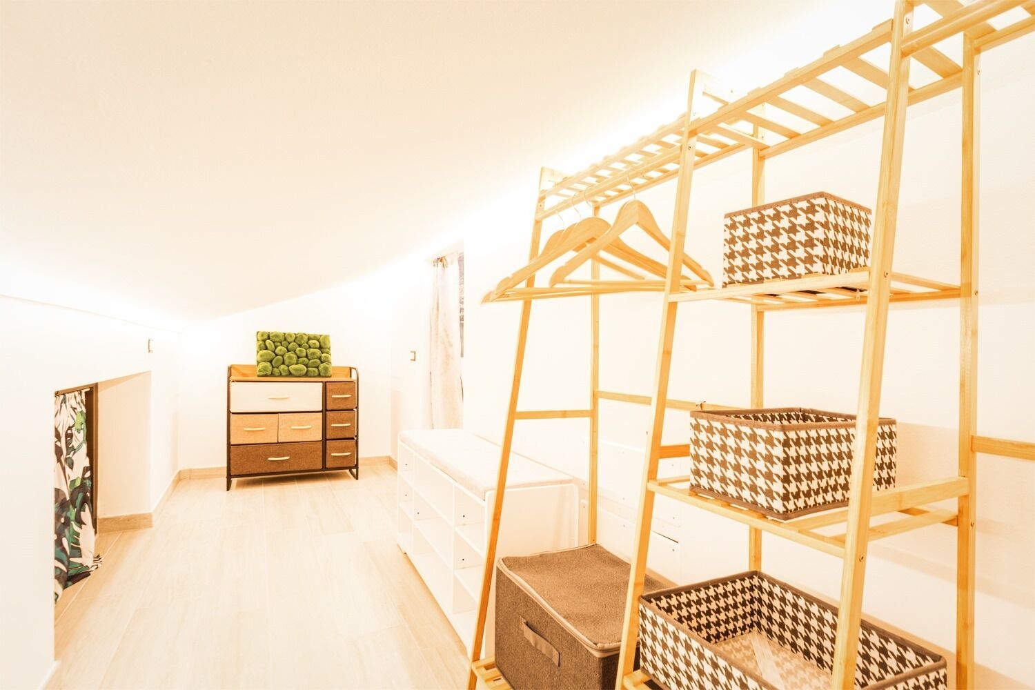 Ein Zimmer mit einem Holzkoffer, einer Kleiderstange und einem Stauraum mit gemusterten Körben.