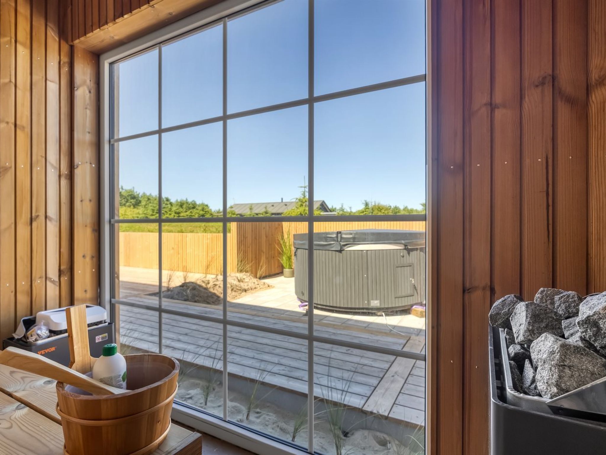 A room with a large window, wooden walls, a hot tub, and a stone feature.