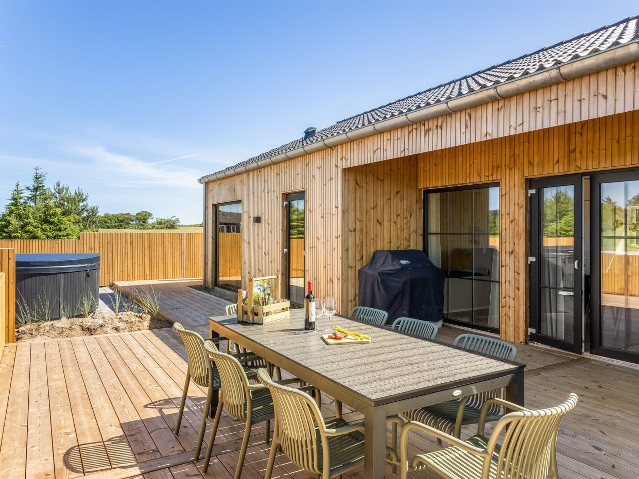 Eine Holzterrasse mit Esstisch, Stühlen, Grill und Whirlpool.