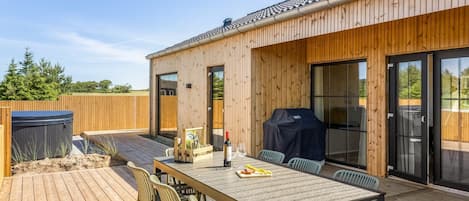 A wooden deck with a dining table and chairs, a barbecue grill, and a hot tub.