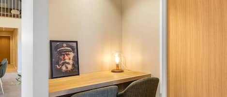 Een kleine werkruimte met een bureau, twee stoelen, een ingelijste foto en een lamp.