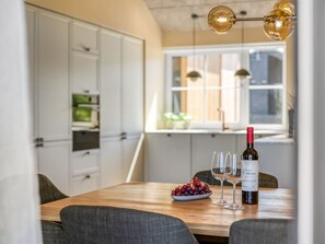 A dining table with a bottle of wine, glasses, and a bowl of grapes in a modern kitchen with white cabinets and a window. - "Indra" - 800m from the sea by Interhome (Løkken)