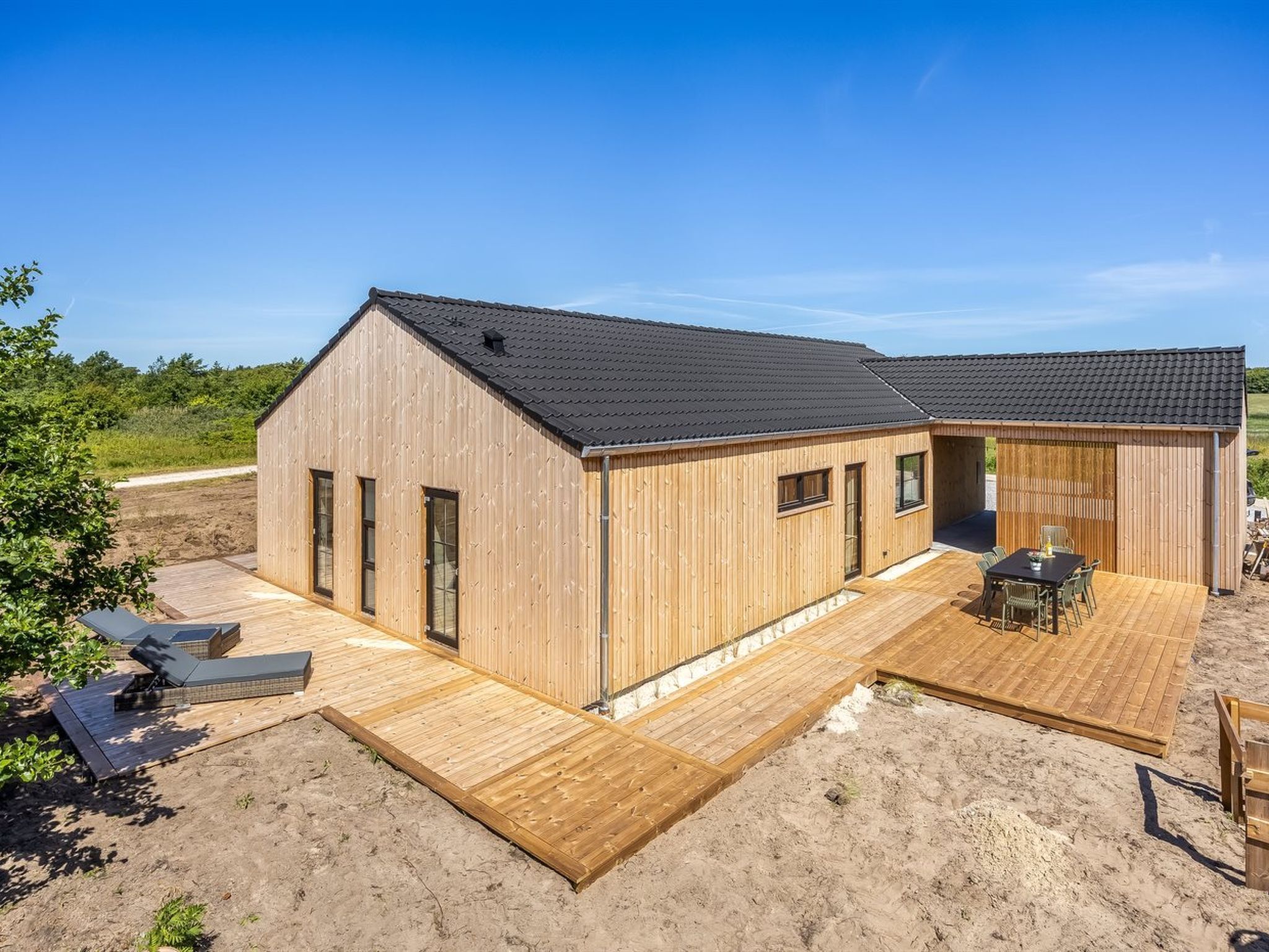 Een houten chalet met terras, een overdekte zitplaats buiten en een onverharde pad ernaartoe.