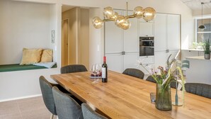 A modern dining area with a wooden table, chairs, a wine bottle, and a decorative vase. - "Indra" - 800m from the sea by Interhome (Løkken)