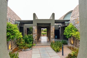 A courtyard with a stone pathway leading to a gate, surrounded by greenery and stone walls.