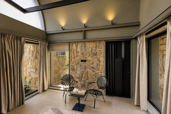A sunlit room with stone walls, a table with chairs, and a view through a glass door.