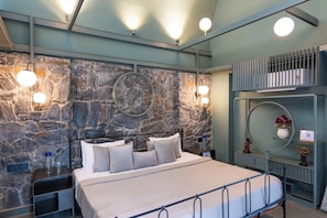 Ein modernes Schlafzimmer mit Steinwand, einem Bett mit vielen Kissen, Nachttischen und einem runden Spiegel an der Wand.