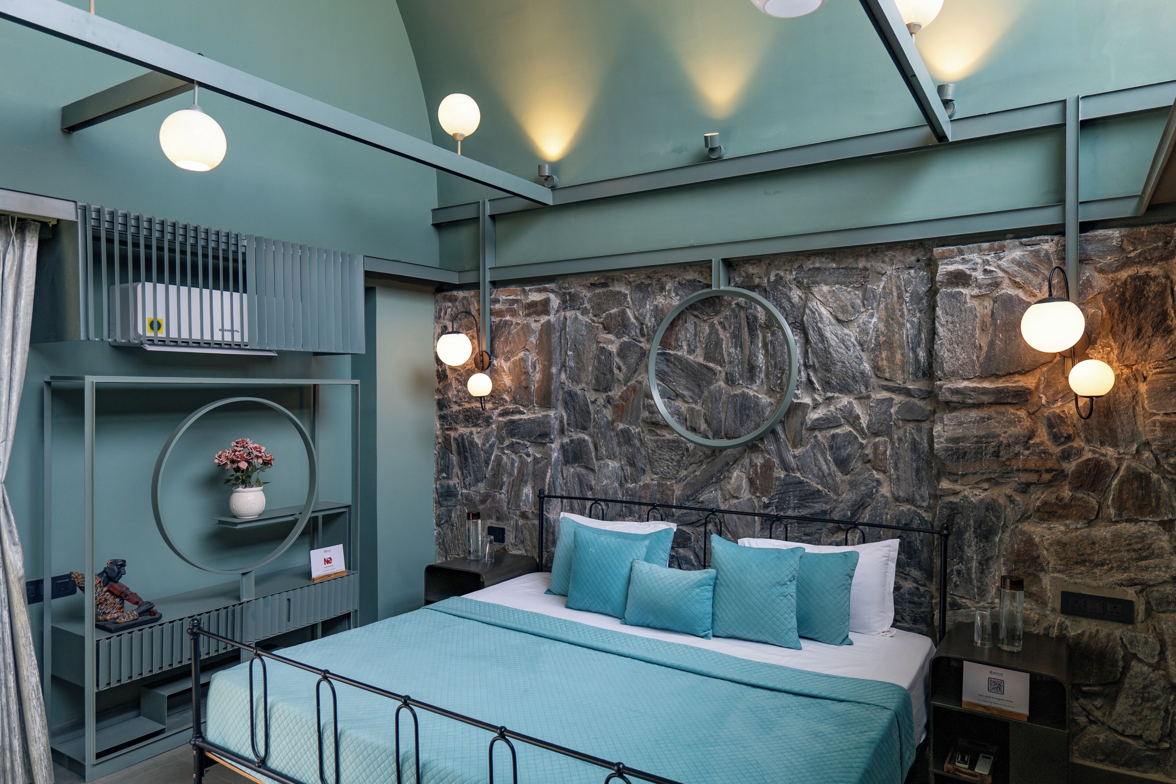A modern bedroom with a stone wall, a bed with blue bedding, and circular wall sconces.